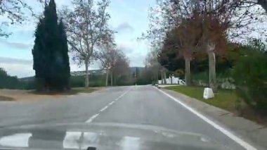 Malaga, İspanya - 24 Ocak 2025 - İspanya 'nın Sotogrande şehrinde ağaçlarla çevrili sessiz bir bölgede boş bir yol. Bulutlu bir gökyüzünün altında karışık palmiye ve yaprak döken ağaçlarla doğal manzara..