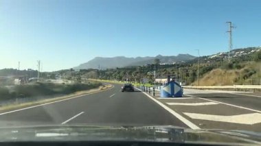 Malaga, İspanya - 24 Ocak 2025 - İspanya 'da manzaralı bir otoyolda giderken, arkasında palmiye ağaçları ve dağlar olan açık mavi gökyüzü ve güneş ışığı altında.