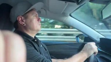 Güneşli bir günde modern bir araba kullanan adam, yola odaklanmış, pencerenin dışında hareket bulanıklığı ve rahat bir iç atmosferi olan.