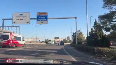 Malaga, İspanya - 24 Ocak 2025 - Mlaga ve Algeciras 'a doğru yol işaretlerinden geçmek, açık mavi gökyüzü ve hava alanı yakınlarındaki güneşli bir günde araçlar.