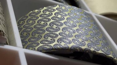 Valmiera, Letonya - 23 Nisan 2025 - Beyaz perakende rafına yerleştirilmiş zarif mavi paisley desenli, ışığı ve doku detaylarını yansıtan katlanmış altın bir kravat.