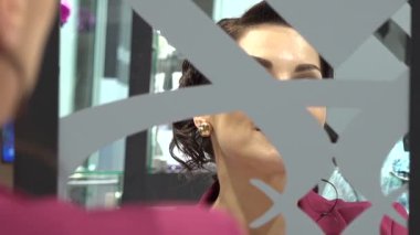 Parlak altın küpeler deneyen bir kadın, parlak, modern bir kuyumcudaki dekoratif aynaya bakarken onları ayarlıyor..