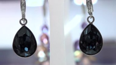 Valmiera, Letonya - 23 Nisan 2025 - İyi ışıklandırılmış bir kuyumcuda beyaz bir stantta sergilenen gümüş kancalı siyah göz yaşı taşı küpelerin yakın çekimi.