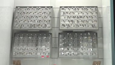 Valmiera, Letonya - 23 Nisan 2025 - İyi aydınlatılmış bir mücevher dolabının içindeki tepsilerde sergilenen çeşitli altın ve gümüş küpeler perakende satışı için düzenlendi ve etiketlendi.