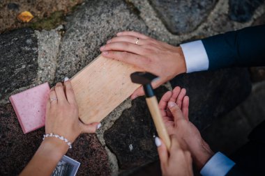 Valmiera, Letonya - 9 Ağustos 2024 - Düğün ritüeli sırasında gelin ve damatların elleri, sembolik birlik töreninin bir parçası olarak tahta bloğa küçük çiviler çakmak