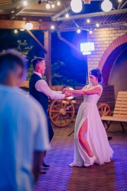 Gelin ve damat halat ışıkları altında neşeyle dans ediyor, gelin rahat etmek için spor ayakkabı giyiyor, eğlenceli ve rahat bir düğün havası yaratıyor..