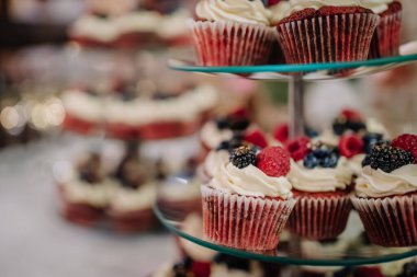 Krem şanti ve ahududu, yabanmersini ve böğürtlen gibi taze böğürtlenlerle kaplı kırmızı kadife kekler sergileniyor..