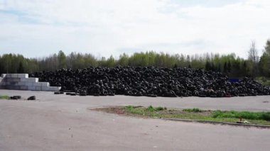 Kudumlar, Letonya - 28 Nisan 2025 - Beton bloklarla çevrili, ağaçlarla çevrili ve açık alanla çevrili bir açık hava geri dönüşüm tesisine yığılmış büyük bir kullanılmış lastik yığını.
