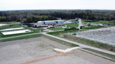 Kudumlar, Letonya - 28 Nisan 2025 - Çevresi orman ve altyapı ile çevrili atık depolama alanı, işleme alanı ve atık konteynırları olan bir atık yönetim tesisinin havadan görüntüsü.