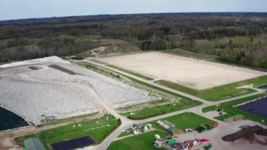 Kudumlar, Letonya - 28 Nisan 2025 - Bulutlu bir gökyüzü altında çoklu atık yönetimi bölümleri, göletler ve yeşil çevreleri olan büyük ve modern bir çöp sahasının havadan görünüşü.