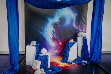 Riga, Letonya - 26 Nisan 2025 - Beyaz kaidesi, mavi kumaşı, taş aksesuarları ve kozmik nebula arkaplanı olan fütüristik uzay temalı sanat kurulumu.
