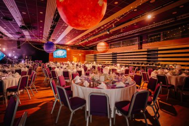 Riga, Letonya - 26 Nisan 2025 - Uzay temalı asılı gezegenler, yemek masaları, mor sandalyeler ve sıcak ortam aydınlatması, editoryal kullanım için hazırlanmış zarif ziyafet salonu. Balta