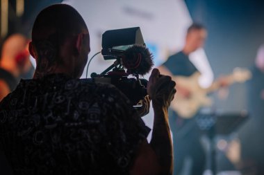 Riga, Letonya - 26 Nisan 2025 - Bir videograf Balta etkinliğinde canlı müzik performansı kaydediyor, loş, atmosferik bir mekanda mikrofonla kameraya odaklanıyor..
