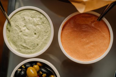 İki kase kremalı soslu yeşil otlu ve bir portakallı baharatlı yemek servisinde karışık zeytinli.