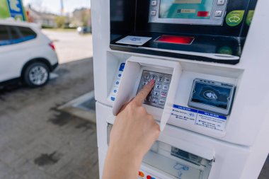 Valmiera, Letonya - 3 Mayıs 2025 - Benzin istasyonu ödeme terminalindeki bir klavyeye PIN kodu giren bir kişi.