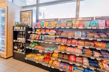 Valmiera, Letonya - 3 Mayıs 2025 - Düzenli perakende raflarda düzenlenmiş çeşitli şeker, çikolata, kurabiye, atıştırmalık ve şarap şişeleriyle dolu bir market koridoru.