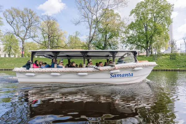 Riga, Letonya - 3 Mayıs 2025 Turistler, yeşil ağaçlarla çevrili açık bir bahar gününde Riga City Kanalı boyunca Samanta 'yı gezerek manzaralı bir gezinti yapıyorlar.