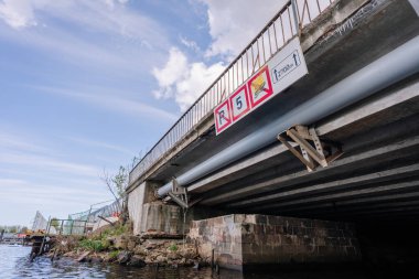 Riga, Letonya - 3 Mayıs 2025 - Paslı korkuluklu Beton köprü hız sınırı, park yasağı ve kayalık bankanın üzerindeki mesafe göstergesi.