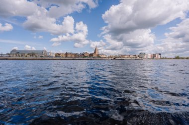 Riga, Letonya - 3 Mayıs 2025 - Rigas 'ın Daugava Nehri' nden gökyüzü bulutlu bir gökyüzü altında merkezi pazar hangarları ve Letonya Bilimler Akademisi 'nin yer aldığı panoramik görünümü