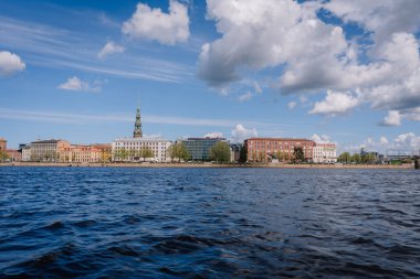 Riga, Letonya - 3 Mayıs 2025 - Daugava Nehri kıyısındaki Rigas eski kasaba manzarası, renkli tarihi binalar ve parçalı mavi gökyüzü altında kilise kuleleri