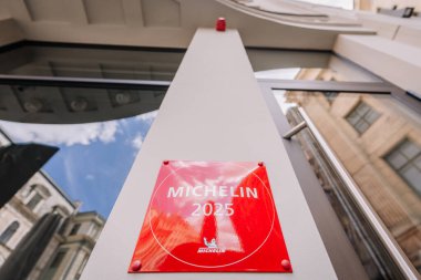 Riga, Letonya - 3 Mayıs 2025 - Kırmızı Michelin 2025 plaketi, aşağıdaki gökyüzü ve mimari yansımalarla modern bir binanın ön cephesine monte edilmiştir..