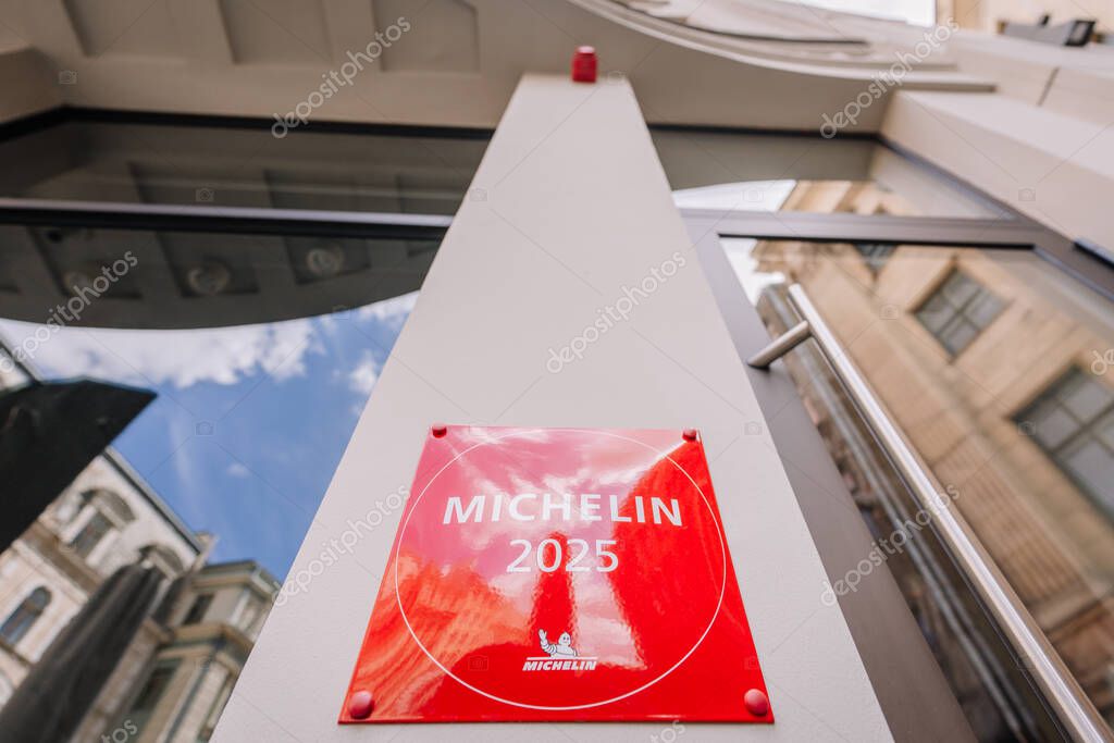 Riga, Latvia - May 3, 2025 - Close-up of a red Michelin 2025 plaque mounted on a modern building facade, viewed from below with sky and architectural reflections.