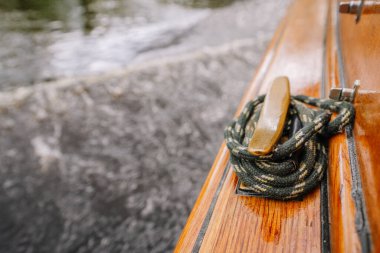 Parlak ahşap bir kayık kenarı üzerinde yeşil bir halatla demirleme halatına yakın plan, bulanık su ve arka planda dalgalar.