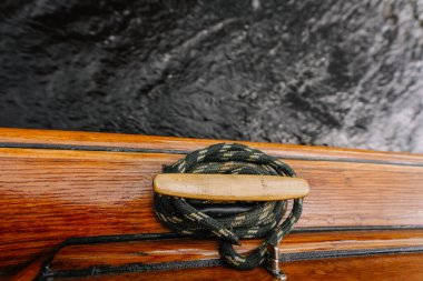 Parlak ahşap bir kayık kenarına sarılı yeşil bir iple donatılmış, arka planda koyu dalgalı su bulunan bir deniz kramponuna yakın plan..
