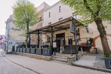 Riga, Letonya - 3 Mayıs 2025 - Old Riga 'daki Black Monks bar ve kafeteryasının dışında tabela, merdiven, teras ışıkları, ağaçlar ve tarihi taş ve alçı duvarlar