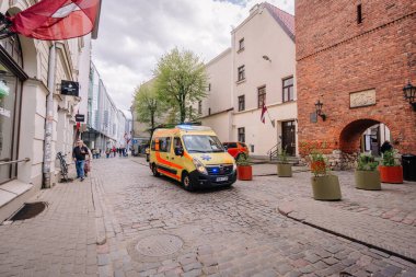 Riga, Letonya - 3 Mayıs 2025 - Litvanya 'nın eski kenti Rigas İsveç Kapısı yakınlarındaki kaldırım taşı caddesindeki ambulans, yayalar, tarihi mimariler ve ekicilerle çevrili.
