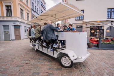 3 Mayıs 2025 - Riga, Letonya 'da kaldırım taşı caddelerinde gezen bir grup insan tepe örtüsü altında sosyalleşirken pedal çeviriyor..