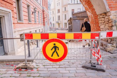 Riga, Letonya - 3 Mayıs 2025 - Yaya yasağı işareti olan şehir şantiyesi ve kaldırım taşlı bir caddede tuğla kemer altında yürüyen bir kadın.