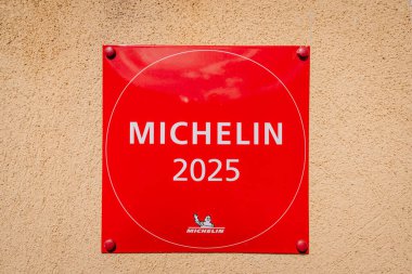 Riga, Letonya - 3 Mayıs 2025 - Bej kaplama duvara asılmış kırmızı Michelin 2025 plaketi aşçılık mükemmelliğini ve restoran tanınmasını temsil ediyor.