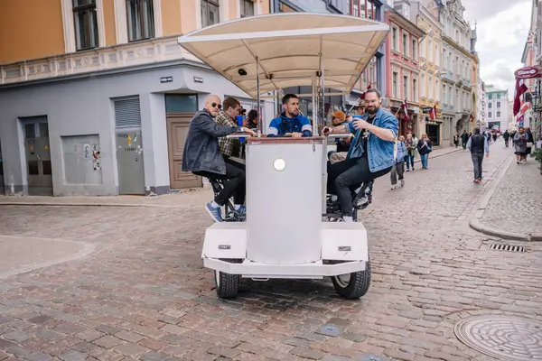 3 Mayıs 2025 - Riga, Letonya 'da kaldırım taşı caddelerinde gezen bir grup insan tepe örtüsü altında sosyalleşirken pedal çeviriyor..