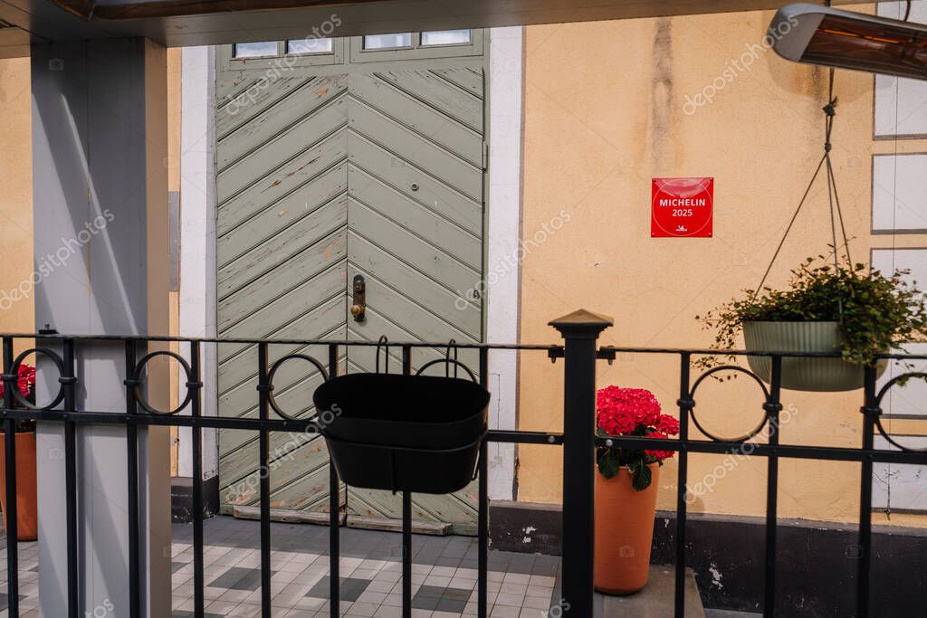 Riga, Latvia - May 3, 2025 - Michelin 2025 plaque on a yellow wall with a rustic green door, patio plants, and metal railing in foreground. Editorial use due to visible branding.