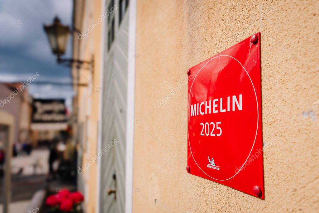 Riga, Latvia - May 3, 2025 - Red Michelin 2025 plaque mounted on a beige wall near a rustic door, with blurred city street and 3 Pavru Restorns sign in background