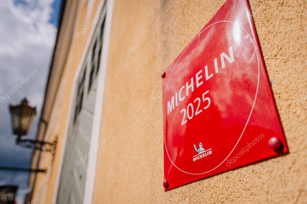 Riga, Latvia - May 3, 2025 - Angled view of a red Michelin 2025 plaque on a yellow wall, with historic street elements like a lamp and door in soft focus. Editorial use only.