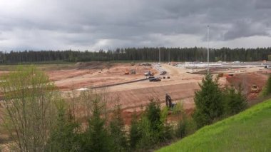 Valmiera, Letonya - 6 Mayıs 2025 - Bulutlu gökyüzü altındaki araçları, ekipmanları ve işçileri ile geniş bir inşaat alanı manzarası.