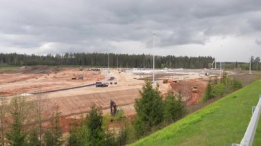 Valmiera, Letonya - 6 Mayıs 2025 - Bulutlu gökyüzü altındaki araçları, ekipmanları ve işçileri ile geniş bir inşaat alanı manzarası.
