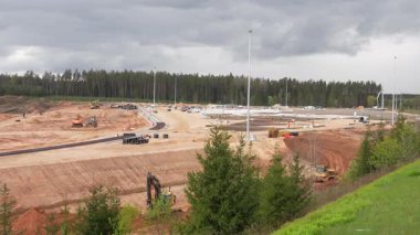 Valmiera, Letonya - 6 Mayıs 2025 - Bulutlu gökyüzü altındaki araçları, ekipmanları ve işçileri ile geniş bir inşaat alanı manzarası.