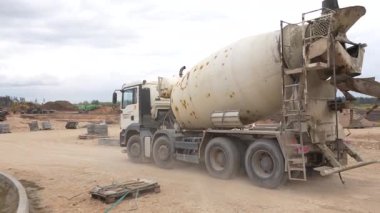 Valmiera, Letonya - 6 Mayıs 2025 - Bir çimento karıştırıcı kamyon toprak yığınları, ağır makineler ve arka planda bulutlu gökyüzü ile büyük bir inşaat alanı boyunca hareket ediyor.