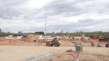 Valmiera, Letonya - 6 Mayıs 2025 - Bulutlu bir gökyüzü altında araçlar, makineler ve malzeme yığınları ile etkin bir inşaat alanının geniş görünümü, altyapı gelişimini gösteriyor.