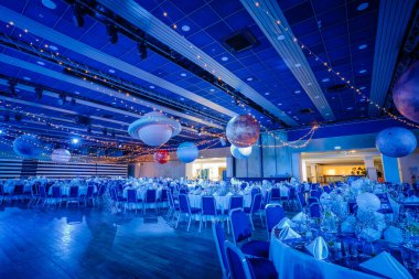 Riga, Letonya - 26 Nisan 2025 - Gezegen temalı tavan dekorlu BALTA galası, mavi ortam aydınlatması, zarif yuvarlak masalar ve akşam kutlaması için parlak bir sahne seti.