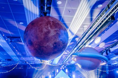 Riga, Letonya - 26 Nisan 2025 - BALTA olayında büyük asılı gezegen süslemeleri ve ışıkları, Satürn ve Mars 'la aydınlık sahnenin üzerinde kozmik bir atmosfer yaratıyor..