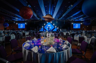 Riga, Letonya - 26 Nisan 2025 - Kozmik temalı BALTA galası asılı gezegenler, sahne ışıkları ve zarif bir akşam kutlaması için düzenlenen yuvarlak ziyafet masaları.