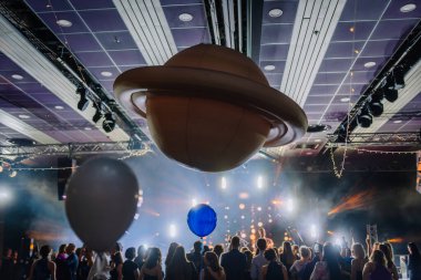 Riga, Letonya - 26 Nisan 2025 - BALTA konserinde kalabalık, neşeli ışıklar, balonlar ve dramatik sahne ışıklandırması üzerinde asılı büyük Satürn aksesuarları uzay temalı bir parti havası yaratır..