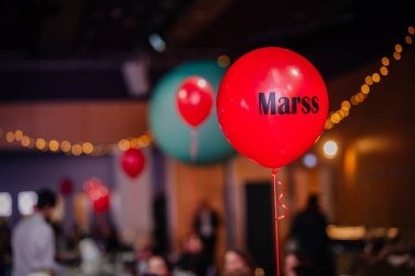 Riga, Letonya - 26 Nisan 2025 - Marss etiketli kırmızı bir balon, yumuşak ışıklar ve şenlikli bir atmosferle çevrili bir BALTA etkinliğinde yüzüyor