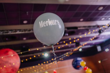 Riga, Letonya - 26 Nisan 2025 - Merkurs etiketli gri bir balon, peri ışıkları ve gezegen temalı dcor ile süslenmiş bir BALTA etkinlik mekanında yüzüyor