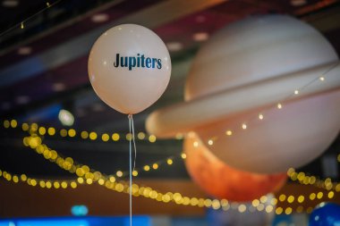 Riga, Letonya - 26 Nisan 2025 - Jüpiter etiketli beyaz bir balon, arka planda sicim ışıkları ve gezegen dekoru olan, galaksi temalı BALTA etkinlik salonunda yüzüyor
