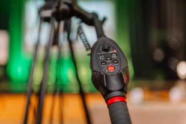 Valmiera, Letonya - 24 Nisan 2025 - Düğmeleri ve kumandası olan, yeşil ışıklı arka planı bulanık bir tripoda monte edilmiş profesyonel bir video kamera sapı denetleyicisi.